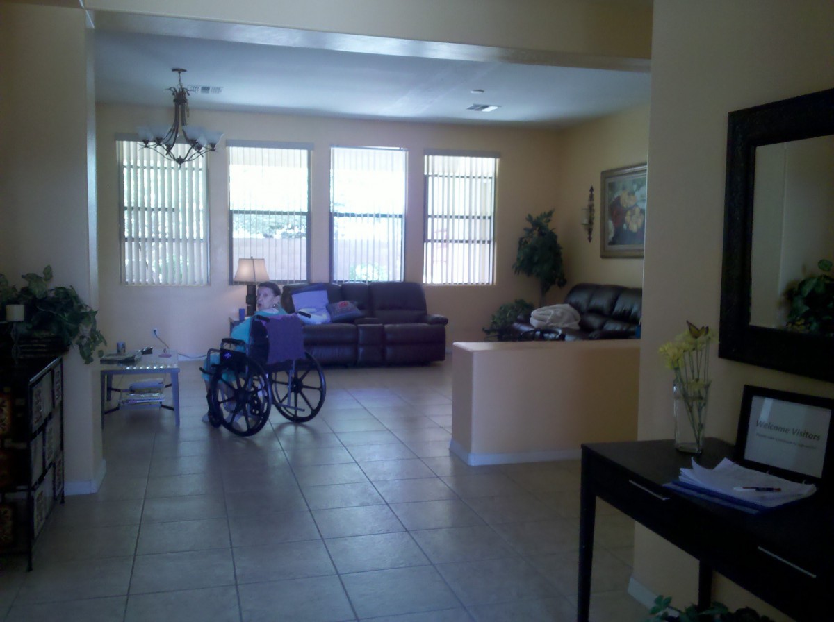 A spacious living room with a sofa, wheelchair, and large windows.