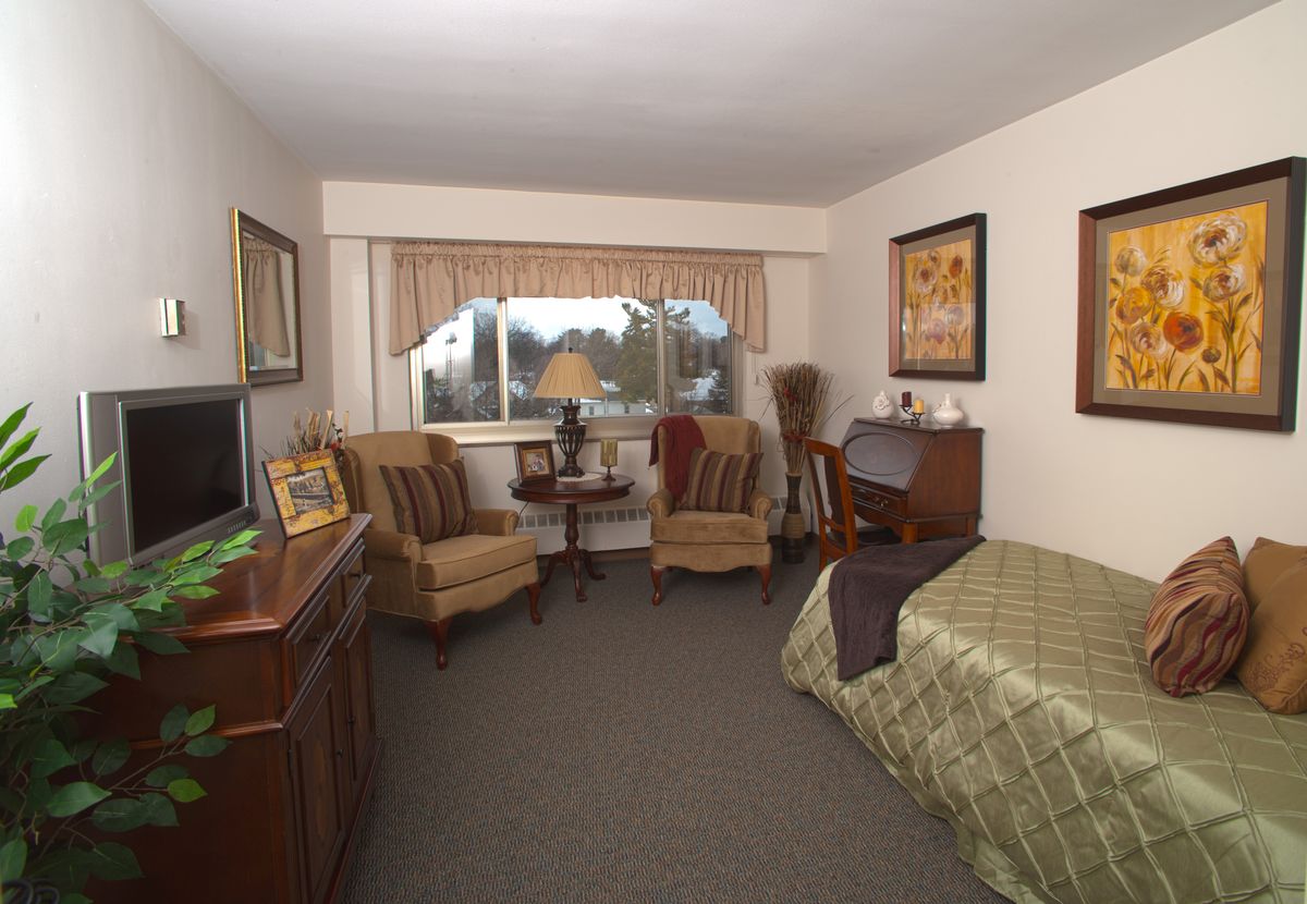 A cozy bedroom with two chairs, a bed, and a large window.