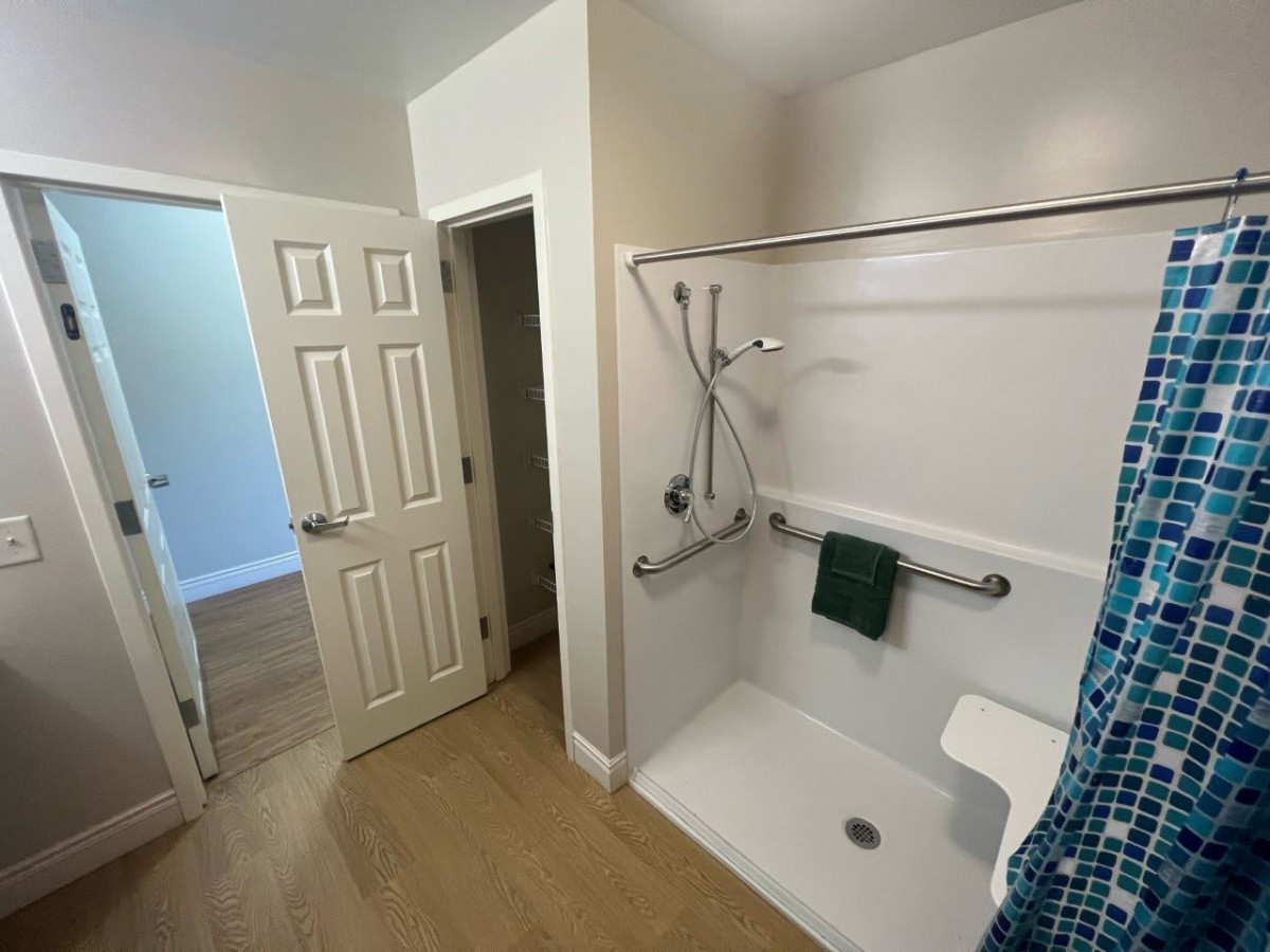 An accessible bathroom featuring a shower with grab bars and an open doorway.