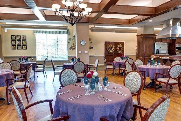 An elegantly set dining room with multiple tables and chairs, featuring a chandelier and soft lighting.