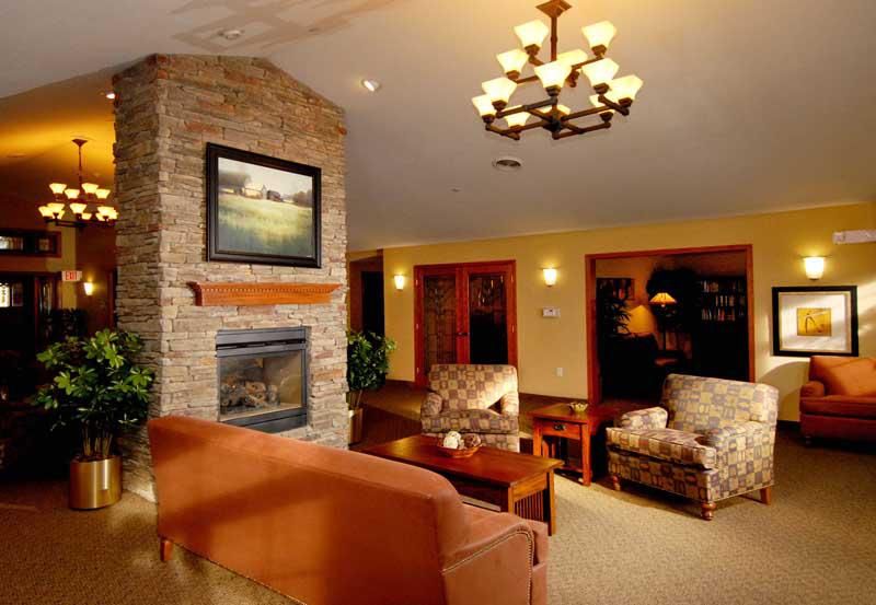 A cozy living room featuring a stone fireplace, comfortable seating, and warm lighting from a chandelier.