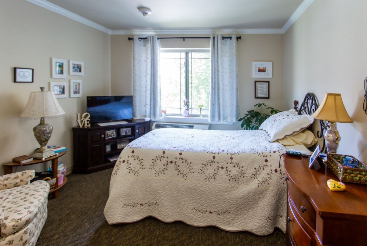 A cozy bedroom with a neatly made bed, television, and window with sheer curtains.