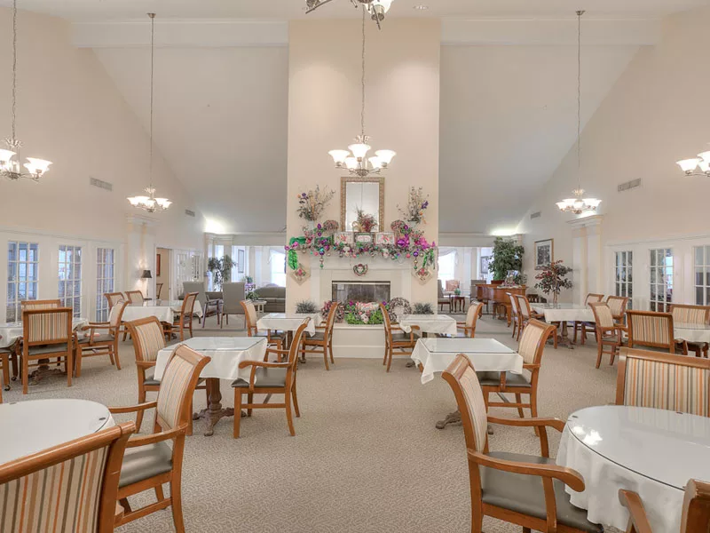 A spacious dining area with elegantly arranged tables and chairs, illuminated by chandeliers.