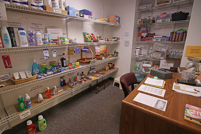 An office supply room with shelves stocked with various items and a desk in the corner.