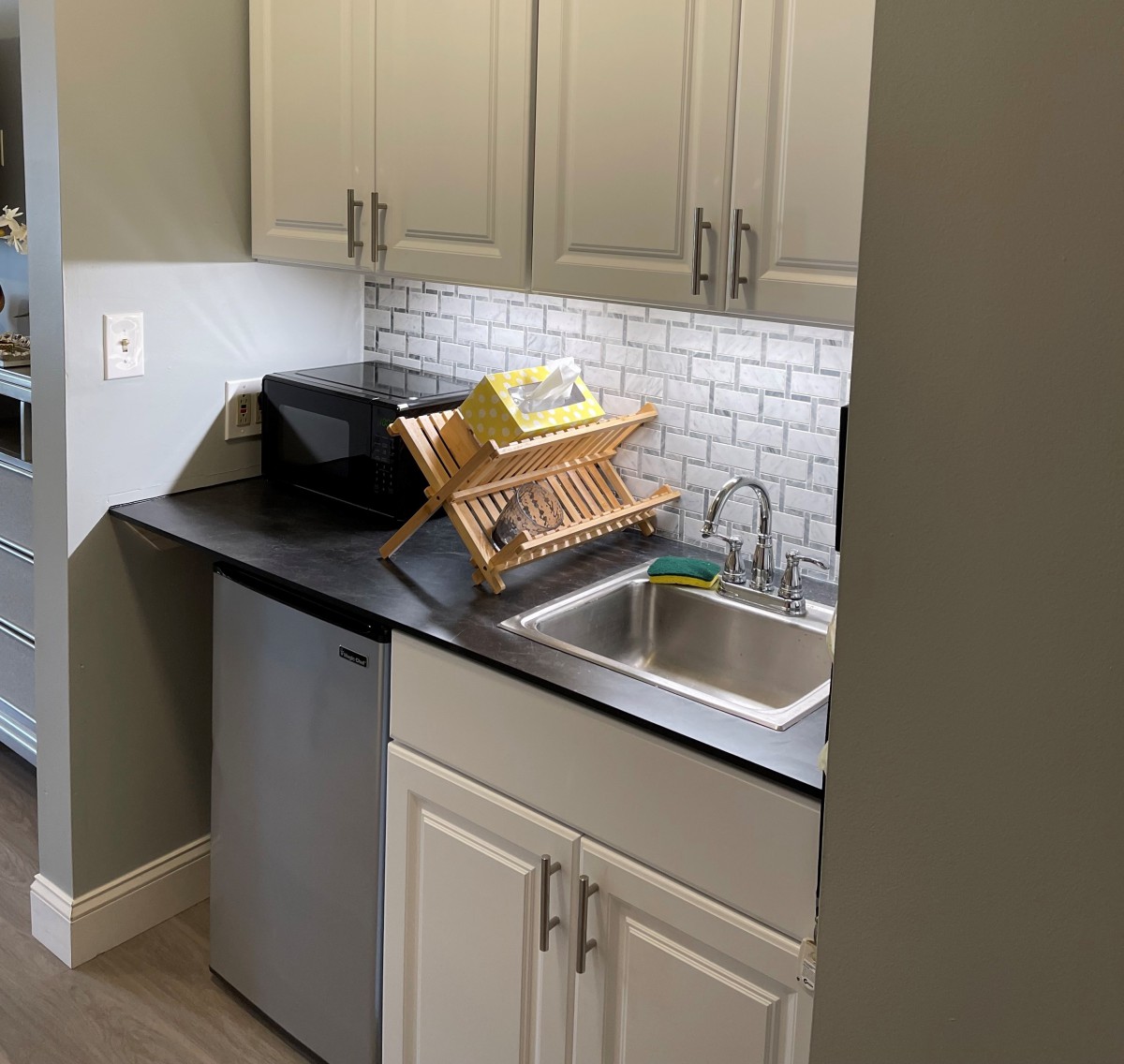 A small kitchen area with a sink, dish rack, and cabinets.