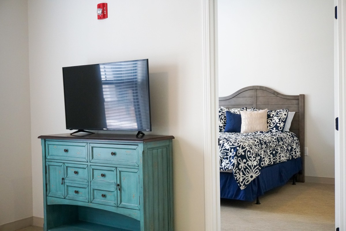 A cozy bedroom with a TV on a teal dresser and patterned bedding in the background.
