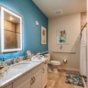 A modern bathroom with a teal accent wall and a backlit mirror.