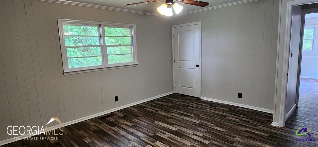 An empty room with wood flooring, a window, a ceiling fan, and a door.