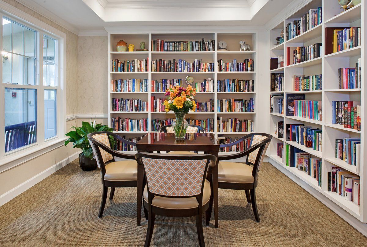 A cozy library corner with a table, chairs, and bookshelves filled with books.