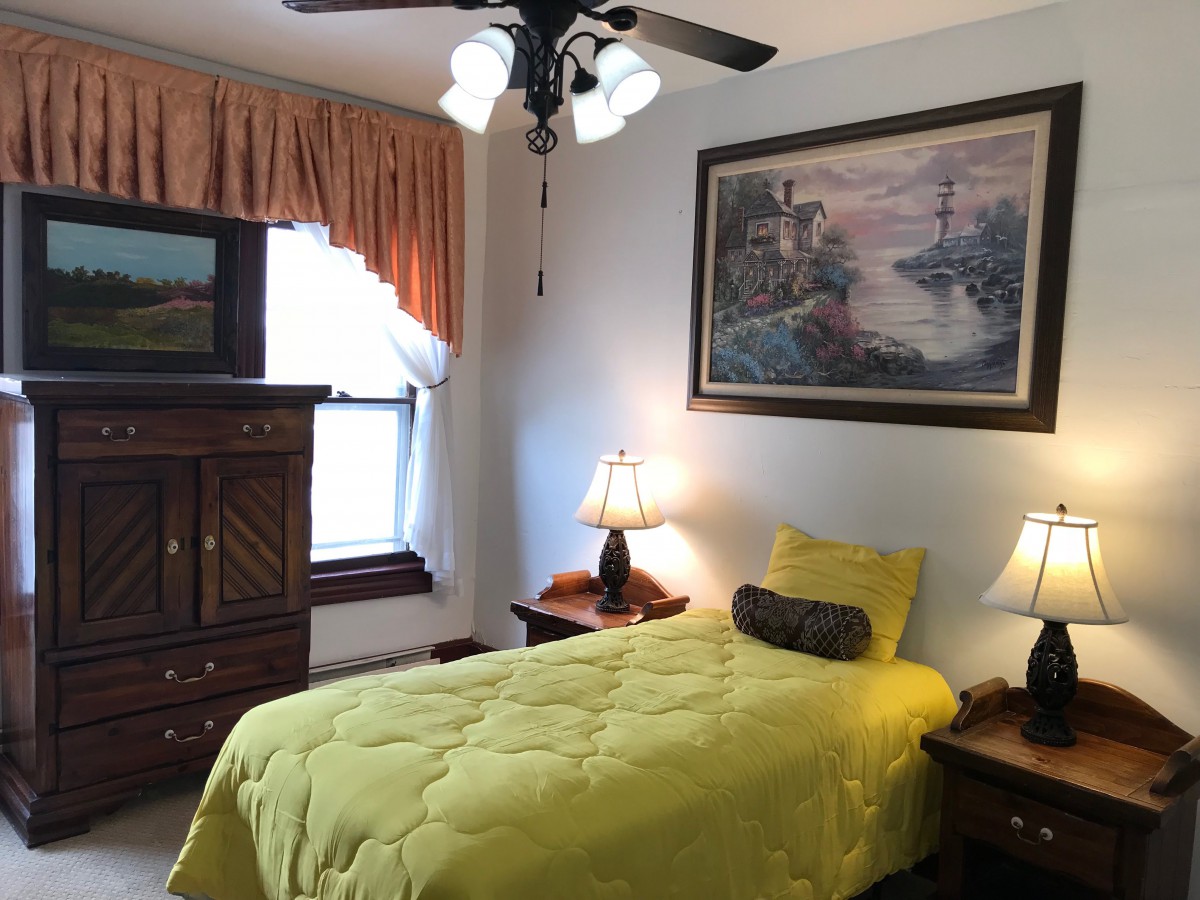 A cozy bedroom with a single bed, bright yellow bedding, and classic decor.
