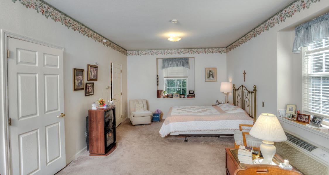 A cozy bedroom with a bed, chair, and various decor elements such as framed pictures and a lamp.
