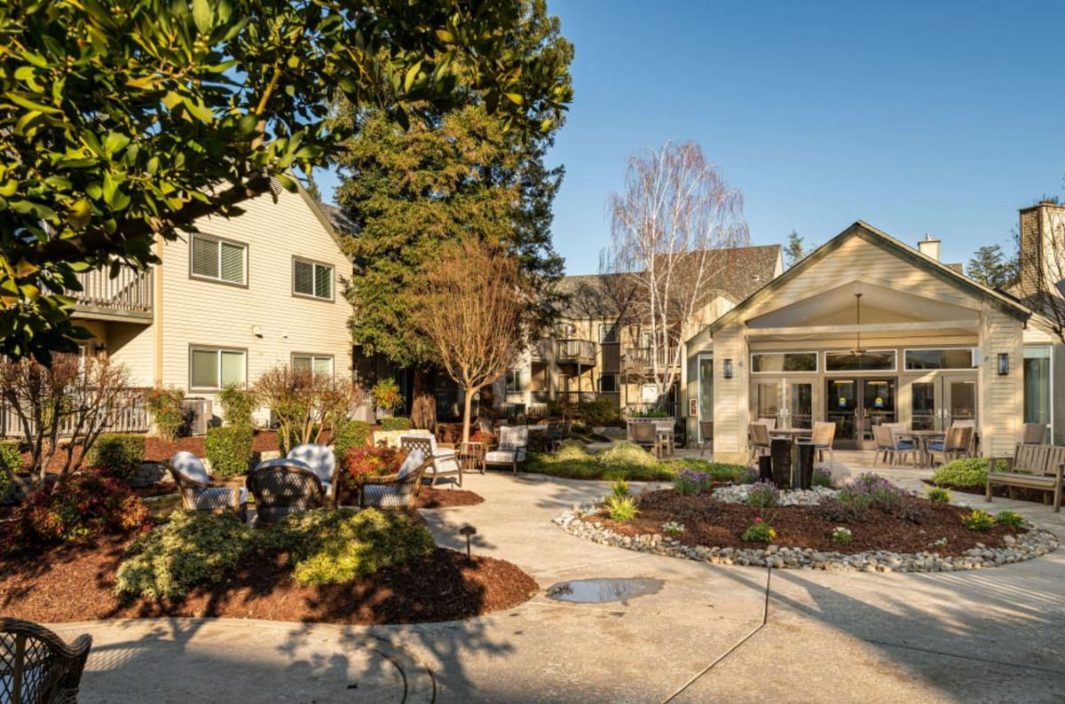 A beautifully landscaped courtyard with outdoor seating, surrounded by buildings and lush greenery on a sunny day.