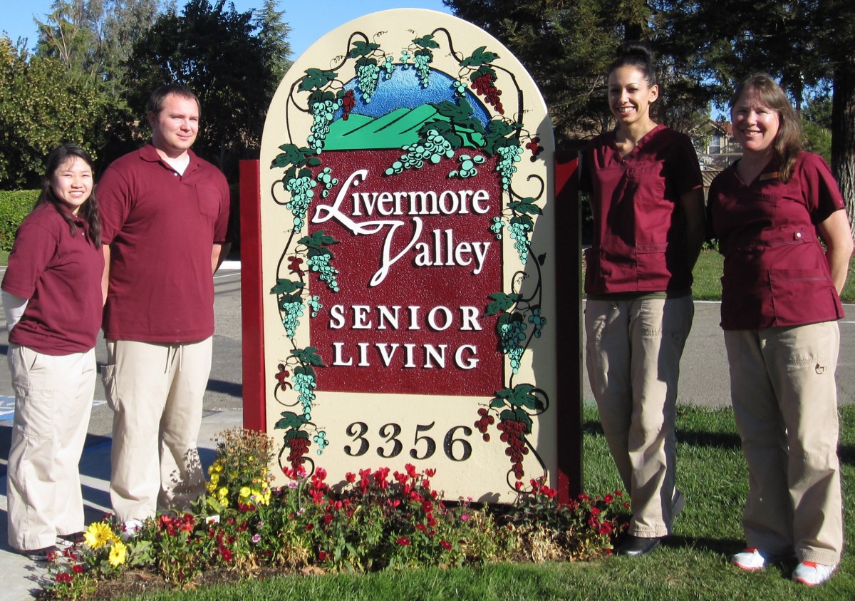 Two people standing next to a Livermore Valley Senior Living sign outdoors.
