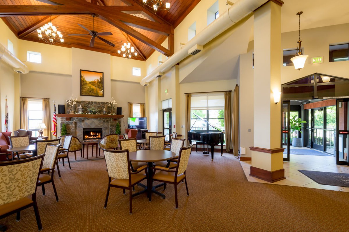 A spacious and elegant lounge with high ceilings, featuring a grand piano and a fireplace.