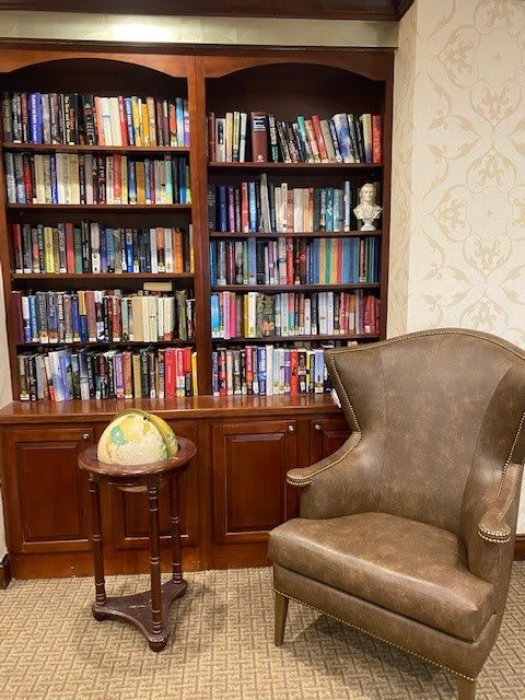 A cozy library corner with a bookshelf filled with books, an armchair, and a globe on a wooden table.