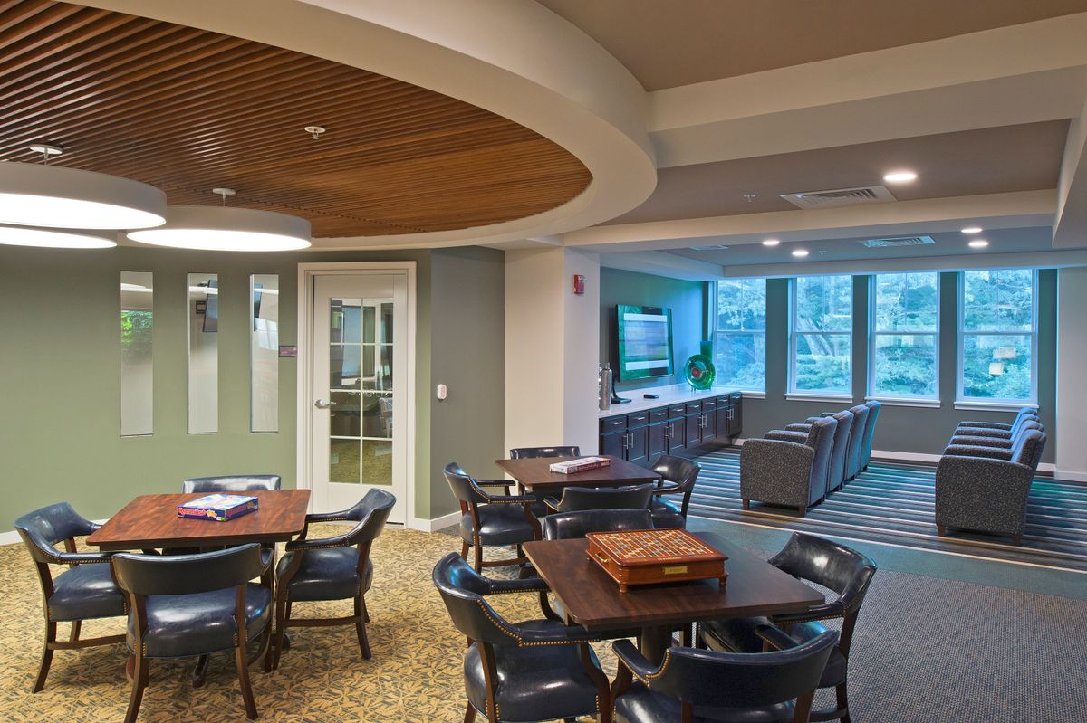 A modern lounge area featuring tables and chairs, with a wooden ceiling and a view of large windows.