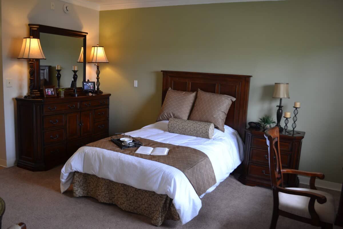 A cozy bedroom with a neatly made bed, accompanied by a lamp and dresser.