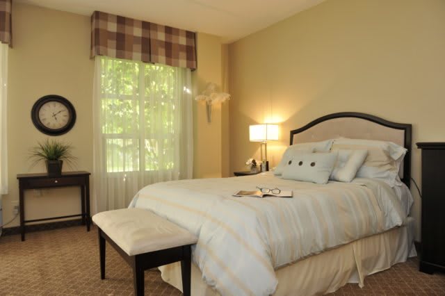 A cozy bedroom interior featuring a comfortable bed, bedside lamp, and window with a scenic view.