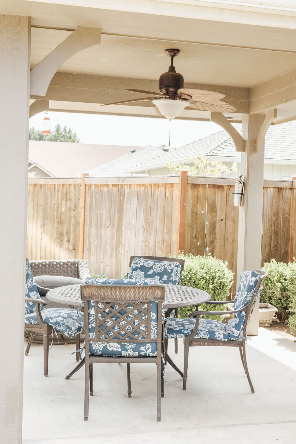 A cozy outdoor patio setup featuring a table and chairs, surrounded by a wooden fence and greenery.