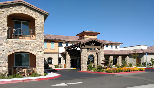 A charming hotel entrance showcasing a blend of stone architecture and vibrant landscaping under a clear blue sky.