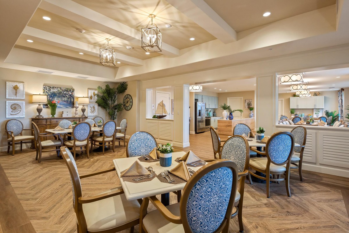 An elegantly decorated dining room with blue upholstered chairs and neatly set tables, featuring warm lighting and sophisticated decor.