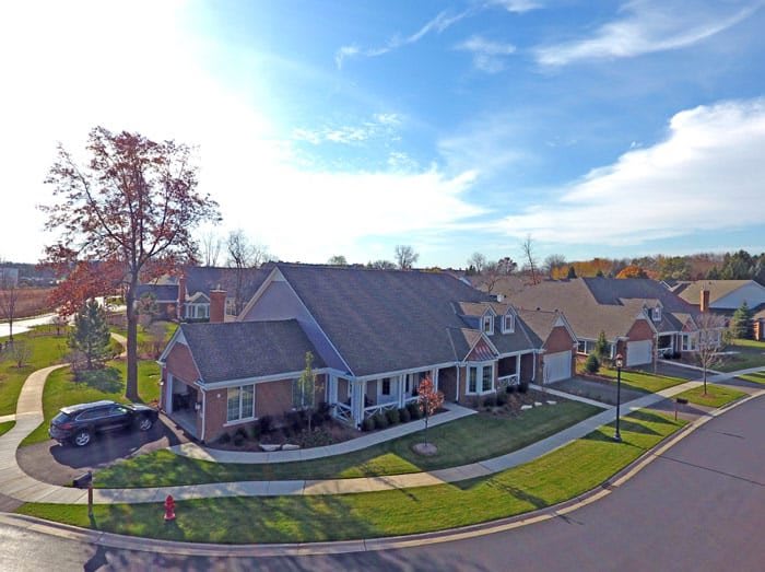 Aerial view of a suburban neighborhood with neatly arranged houses and well-maintained lawns under a bright blue sky.