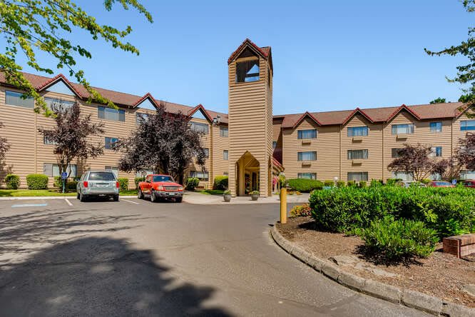 A hotel building with a parking lot and cars in front, surrounded by trees.