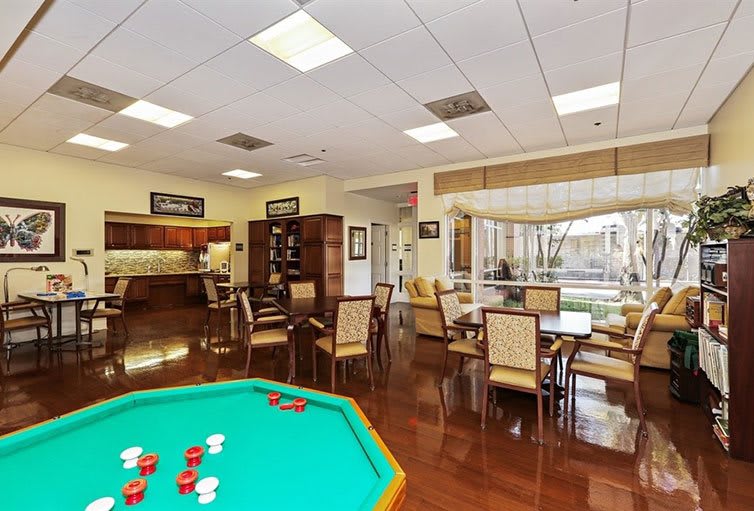 A spacious game room featuring a poker table and multiple seating areas under bright lighting.