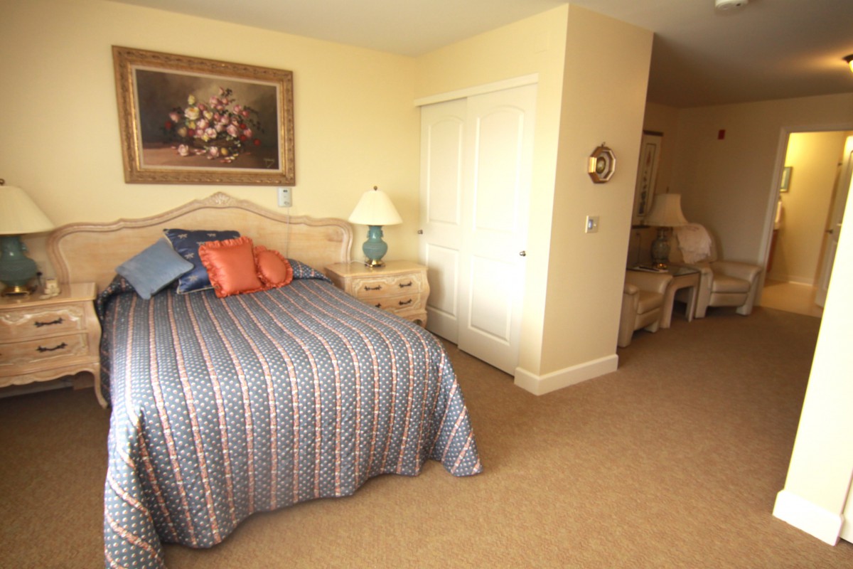 A cozy bedroom with a patterned bedspread and decorative pillows, featuring wooden furniture and warm lighting.