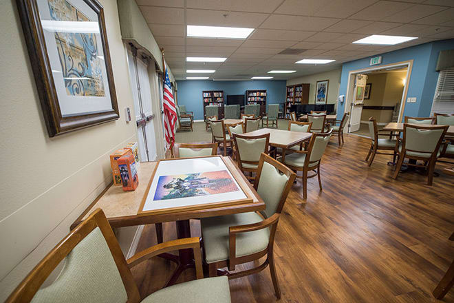 A well-lit room with several tables and chairs, featuring wooden flooring and an American flag in the corner.