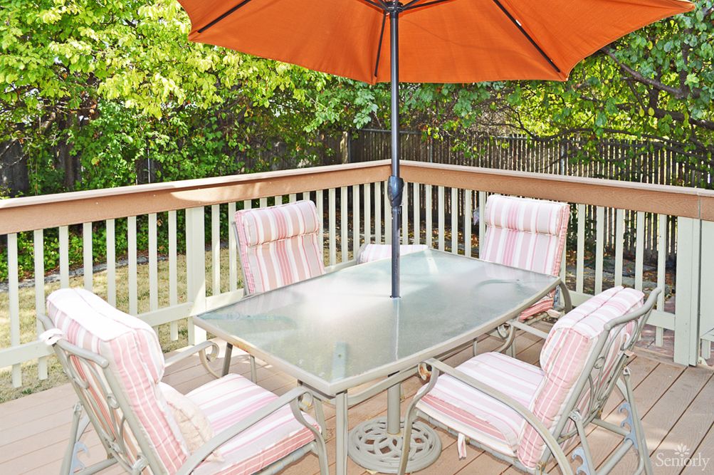 A patio setup with a glass table, cushioned chairs, and an orange umbrella on a wooden deck.