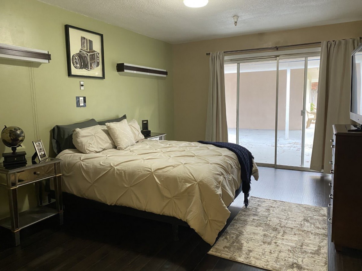 A cozy and minimalist bedroom with a comfortable bed, light green walls, sliding glass doors, and simple decor.