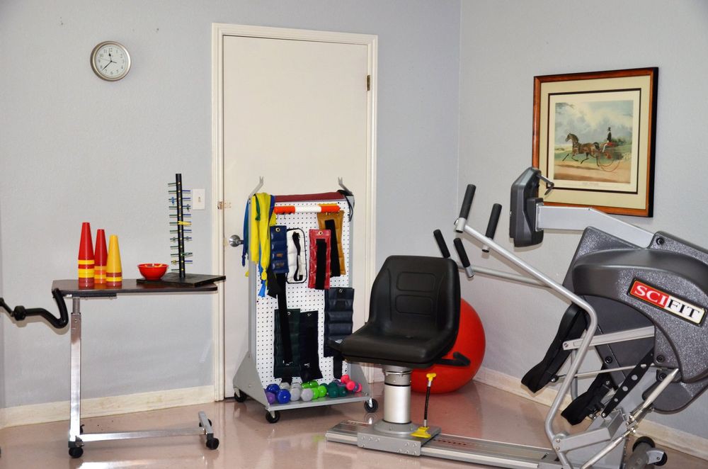 A physiotherapy or fitness room with various exercise equipment including a stationary bike, resistance bands, and weights.