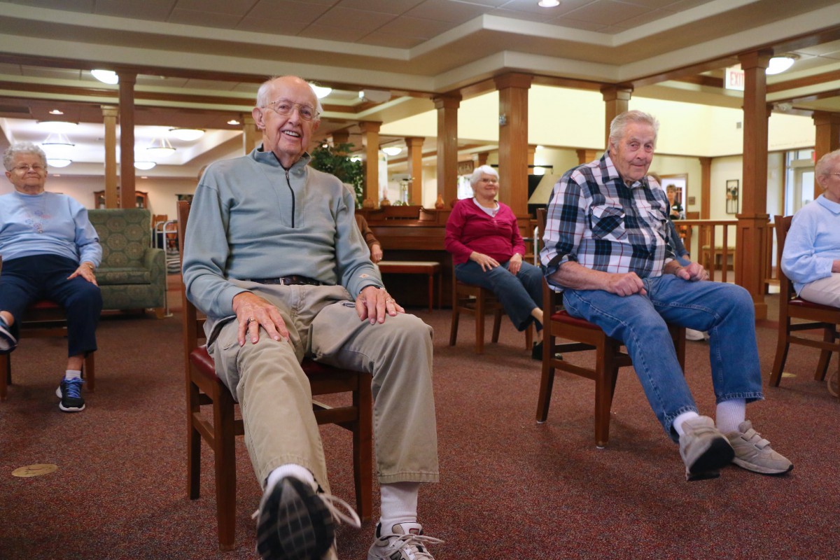 A group of elderly individuals participating in a seated exercise session indoors.