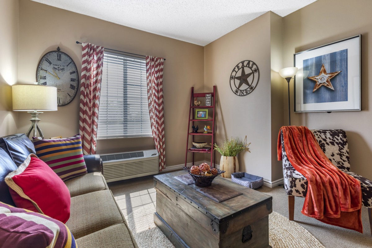 A cozy living room with a clock on the wall, comfortable couch, rustic coffee table, and a ladder shelf filled with decor.