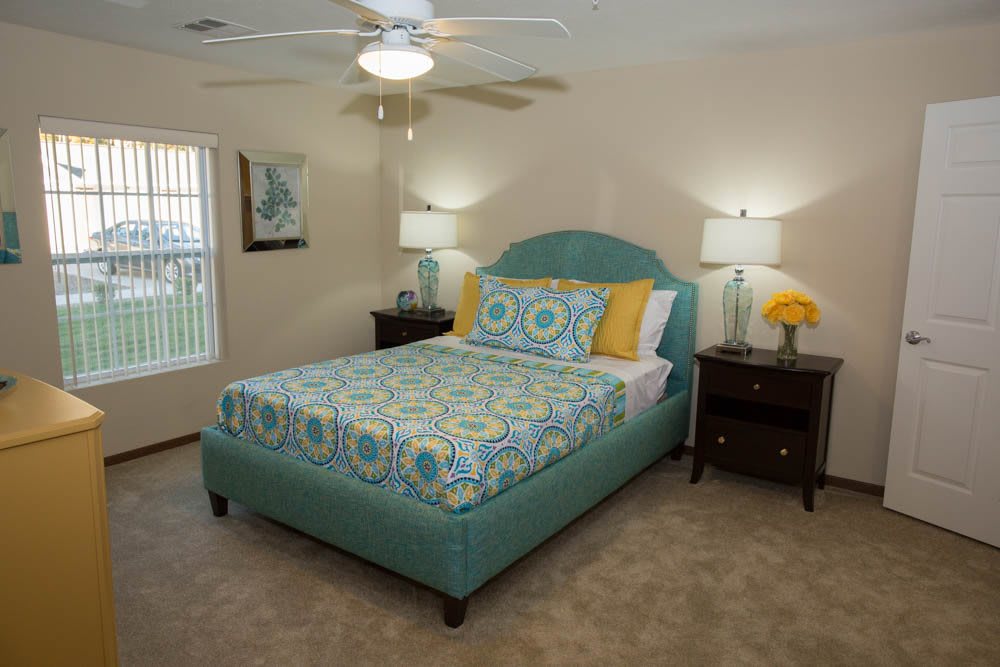 A cozy bedroom with a colorful bedspread, twin lamps on bedside tables, and a ceiling fan.