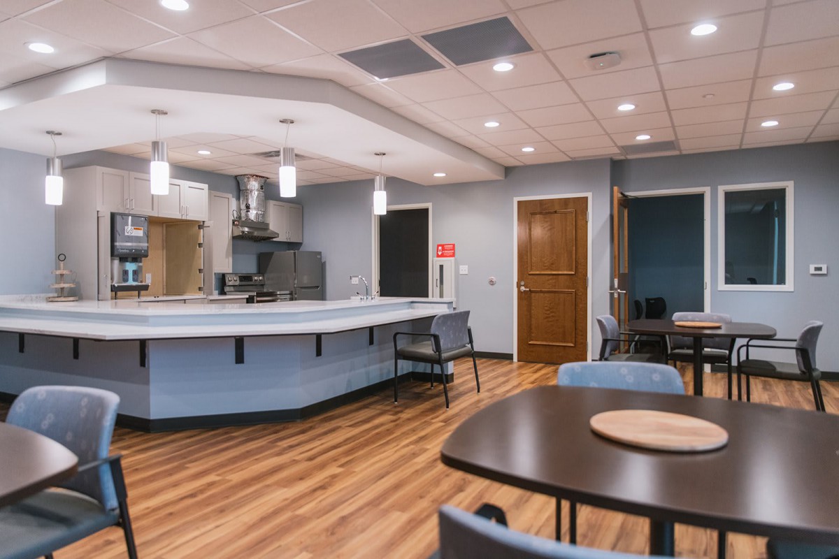 A modern kitchen and dining area with wood flooring, featuring a central island, pendant lighting, and several tables and chairs.