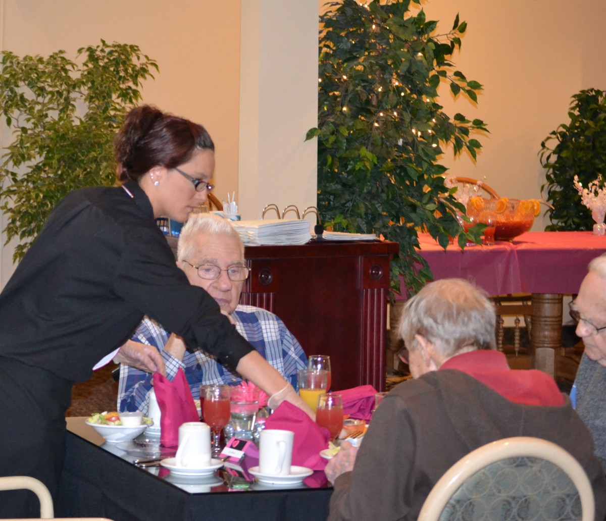 A waitress serving drinks to elderly patrons at a restaurant.