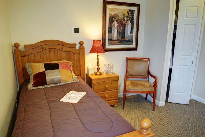 A cozy bedroom with a wooden bed, nightstand, and a decorative lamp, complemented by wall art.
