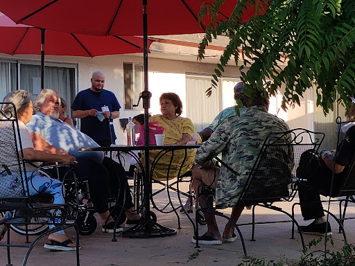 A group of elderly individuals enjoying a pleasant afternoon conversation under red umbrellas.