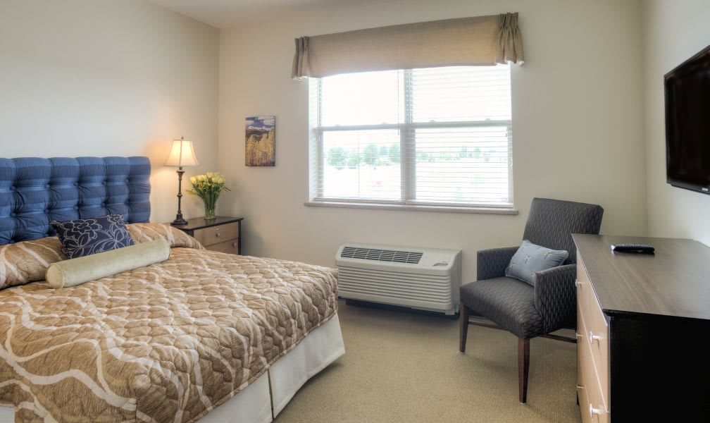 A cozy, minimalist bedroom with a neatly made bed, a comfortable chair, and a large window allowing natural light to illuminate the space.