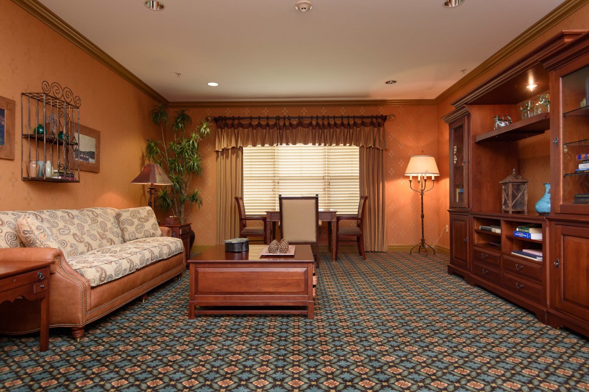 A cozy living room with classic decor, featuring a patterned carpet, a sofa, a wooden coffee table, and a large window with curtains.