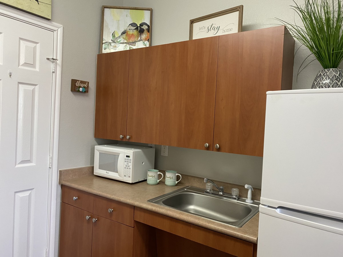 A small kitchen area with a microwave, sink, and wooden cabinets.
