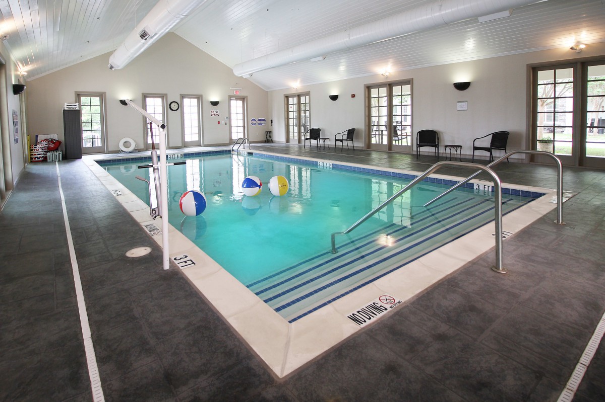 An indoor swimming pool with beach balls floating, surrounded by seating and large windows.
