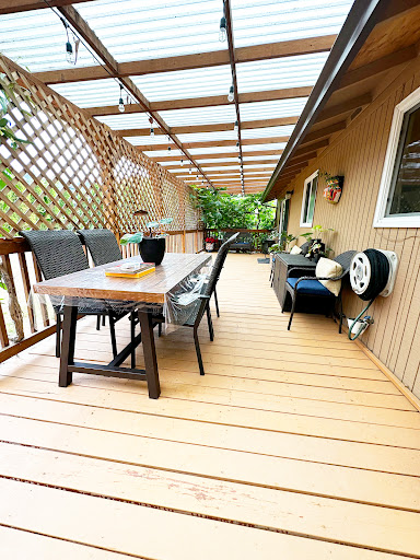 A cozy outdoor deck featuring a wooden table, comfortable seating, and beautiful greenery.