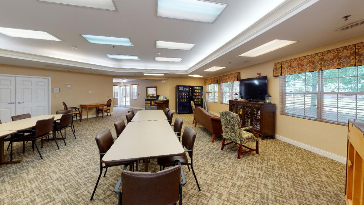 A spacious community room with tables and chairs arranged for meetings, featuring a TV and comfortable sofas.