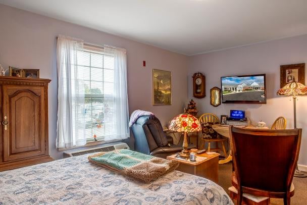A cozy bedroom with a desk setup, featuring a window, lamp, and comfortable furnishings.