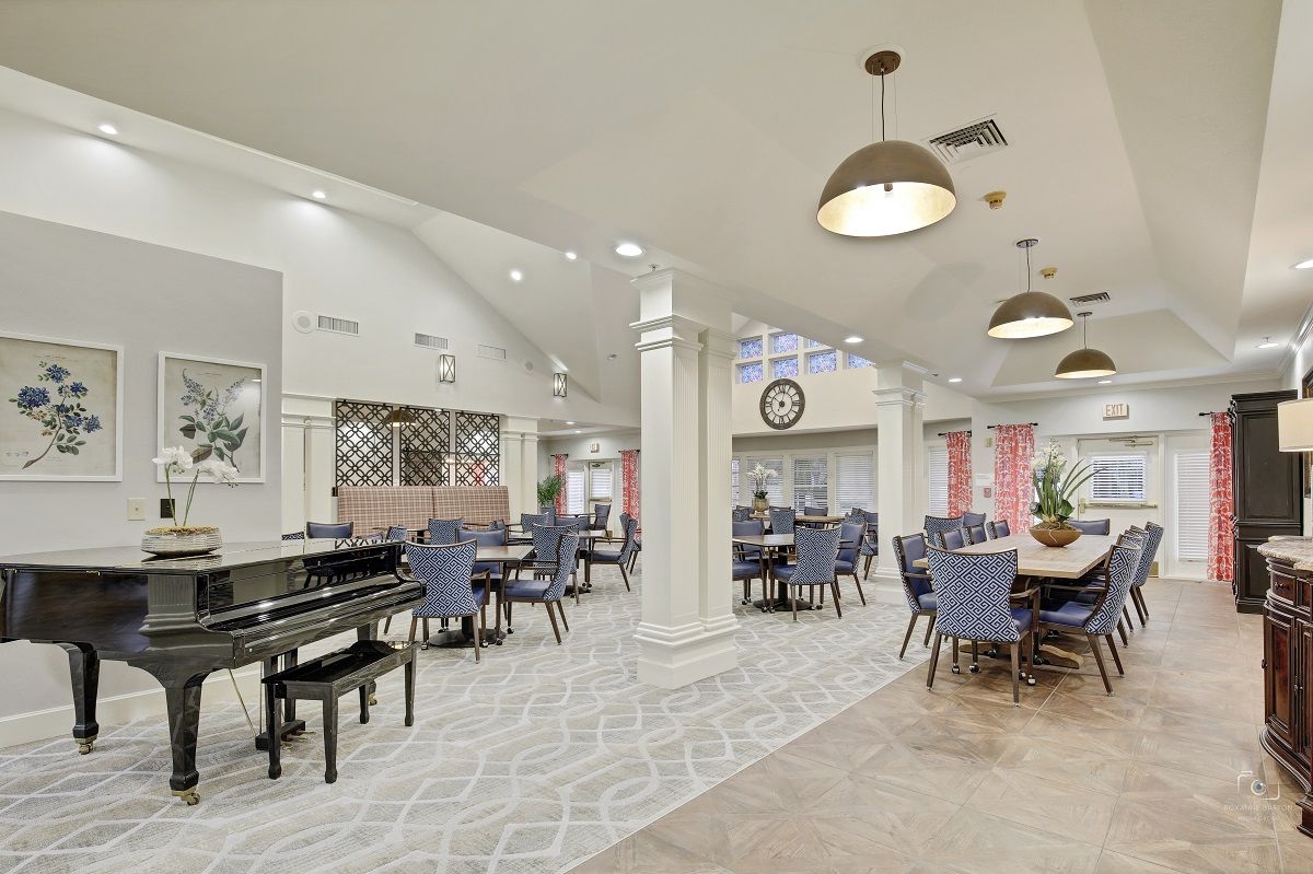A spacious and elegantly decorated dining area featuring neatly arranged tables and chairs, a grand piano, and stylish chandeliers.