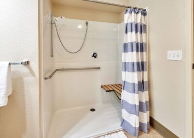 An accessible shower with a striped curtain, bench seat, and grab bar.