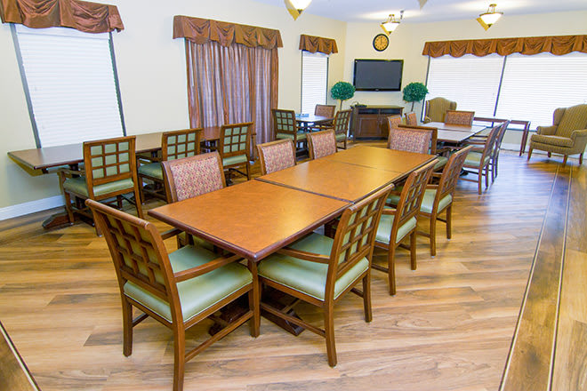 A well-arranged dining room with wooden tables and chairs, featuring a television and decorative elements in the background.